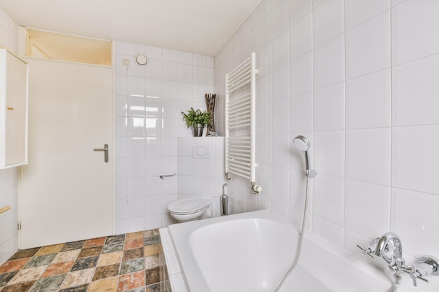 Witte badkuip met metalen kraan tegen toilet dicht bij de deur in moderne badkamer in minimalistische stijl in appartement