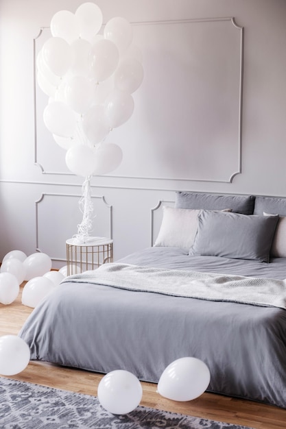 Witte ballonnen in stijlvolle grijze slaapkamer met comfortabel kingsize bed met grijs beddengoed en deken echte foto met kopieerruimte op de lege muur