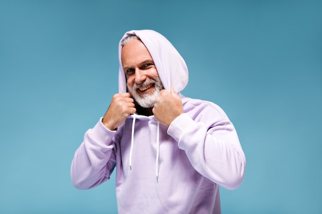 Witte bebaarde man in hoodie glimlachend op blauwe muur