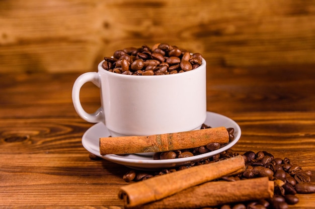 Foto witte beker gevuld met koffiebonen en kaneelstokjes op een houten tafel