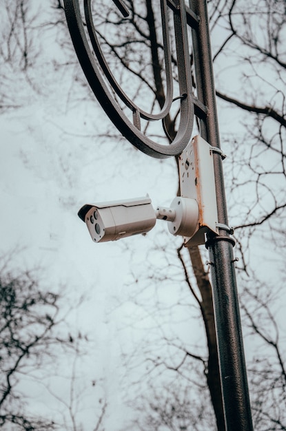 Witte bewakingscamera opknoping op een paal. De camera kijkt naar de volgorde in de straten en in de parken. Camera op een post in een park. Zijaanzicht en recht