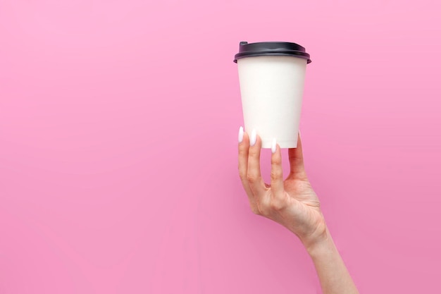 Witte blanke papieren kop koffie in de handen van een vrouw op een roze geïsoleerde achtergrond