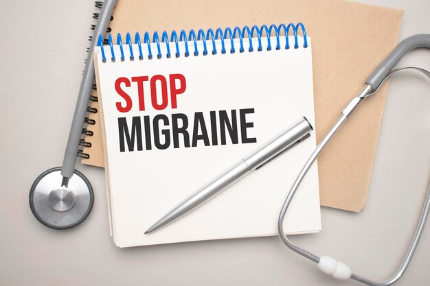 Witte blocnote met de woorden STOP MIGRAINE en een stethoscoop op een blauwe achtergrond. medisch concept