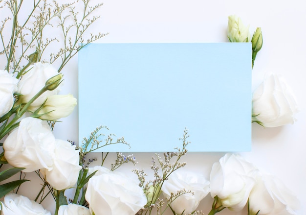 Witte bloemen en lichtblauw rechthoekig papier op een wit bovenaanzicht
