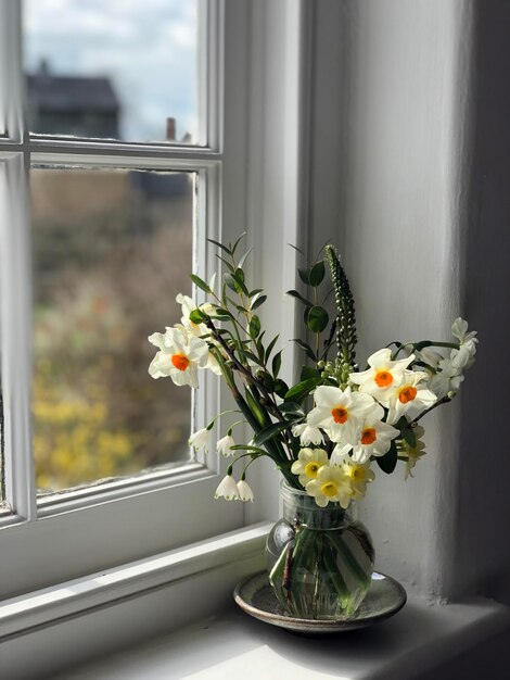 Witte bloemen in een glazen pot bij het raam