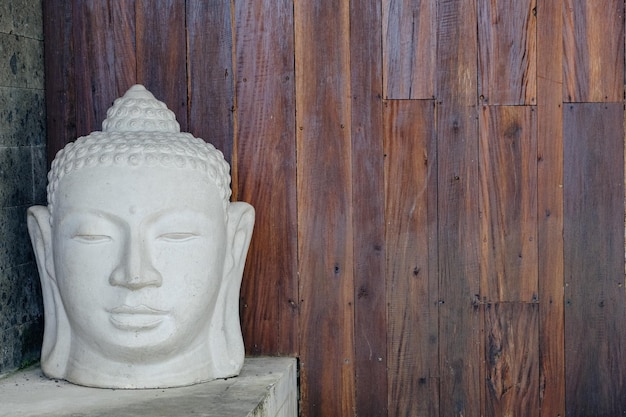 Witte Boeddha-hoofdstatue die rust voor een verticale houten plankmuur