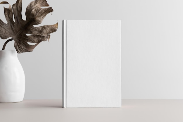 Witte boek mockup met een monstera blad in een vaas op een beige tafel