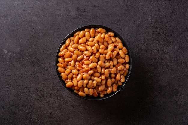 Witte bonen in tomatensaus in kom op zwarte leiachtergrond