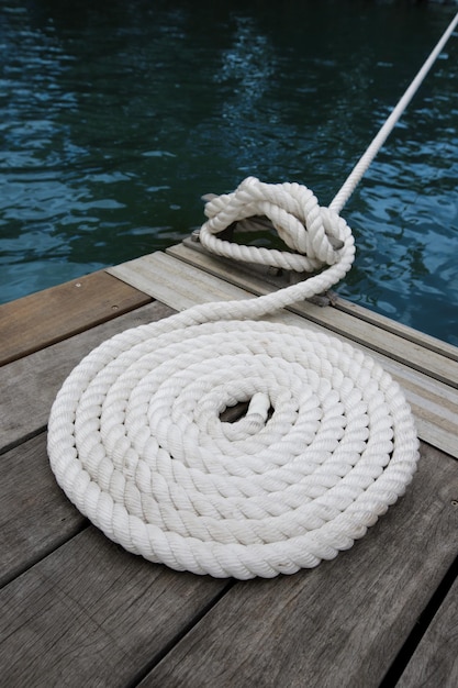 Foto witte boot touw bevestigd aan een houten dok met donker water eronder