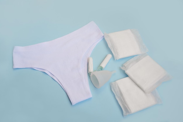 Witte broek met maandverband tampons menstruatiecup op blauwe achtergrond Concept van critical