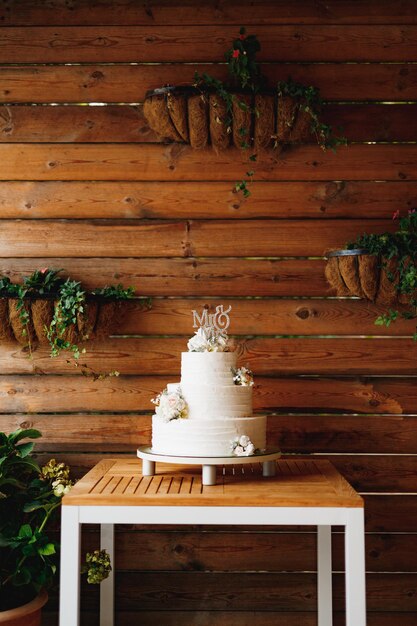 Witte bruidstaart met drie niveaus staat op een tafel tegen een houten muurachtergrond