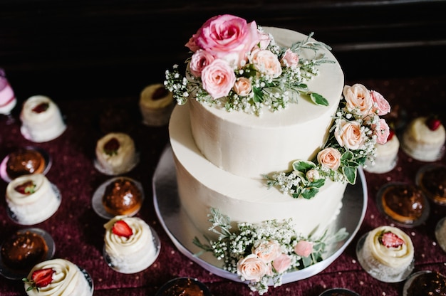 Witte bruidstaart met roze bloemen en Groenen op een feestelijke tafel