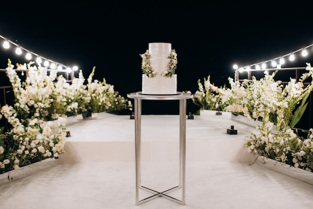 Witte bruidstaart op een hoge stand bij het witte podium met groen decor