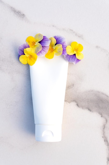 Witte buis met cosmetisch product met viooltjesbloemen op marmeren achtergrond Crème buis hydraterend schuim en sunblock Professioneel huidverzorgingsconcept Kopieer ruimte Reclame