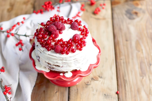 Foto witte cake met rode bessen en een tak op een houten tafel