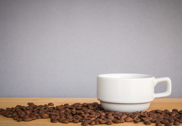 Witte coffekop en koffiebonen op houten bureau met grijze achtergrond