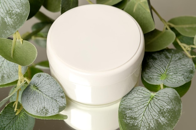 Foto witte container met cosmetische crème op een spiegeloppervlak met eucalyptusbladeren