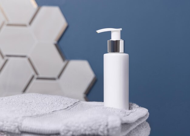 Witte cosmetische fles op lichtgrijze handdoek tegen blauwe en grijze muur in badkamer mockup