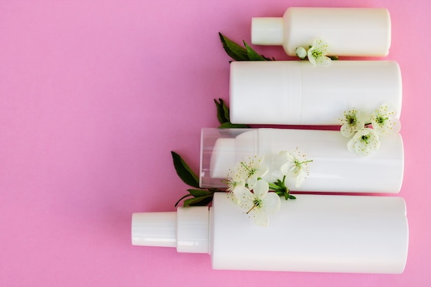 Witte cosmetische flessen, badbom, handgemaakte zeep, badzout, massageborstel, spons, wattenstaafjes met kersenbloemen op een roze achtergrond. Natuurlijke biologische cosmetica concept.