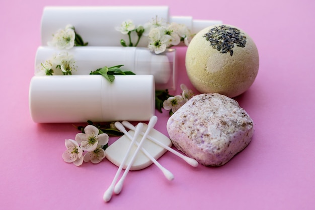 Witte cosmetische flessen, badbom, handgemaakte zeep, badzout, massageborstel, spons, wattenstaafjes met kersenbloemen op een roze achtergrond. Natuurlijke biologische cosmetica concept.