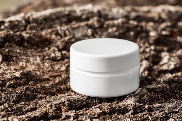 Witte cosmetische pot met verstevigende crème op ruwe boom schors oppervlak vertoning crème mock up merk