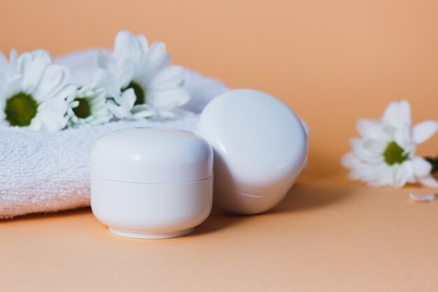 Witte cosmetische tubes met gezichtscrème op een beige achtergrond met witte bloemen