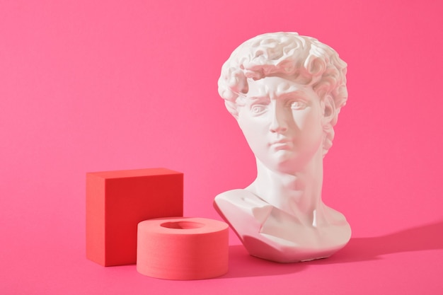 Foto witte decoratieve sculpturale buste en verschillende roze geometrische onderzetters op een roze achtergrond