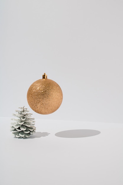 Witte dennenappel met gouden glanzende kerstbal zwevend op witte achtergrond Minimale vakantie