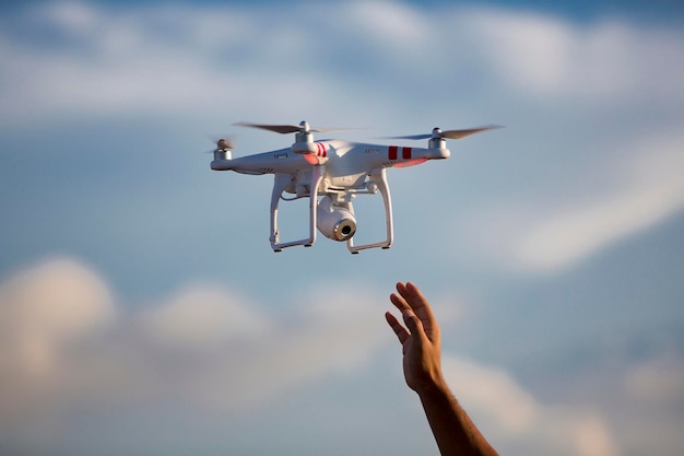 Witte drone zweeft in een helderblauwe lucht met de hand klaar om hem te vangen