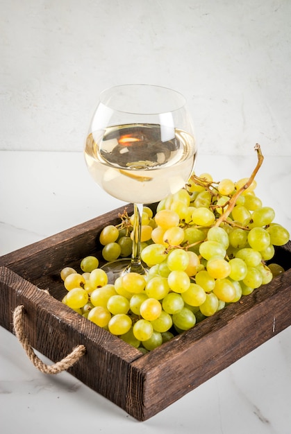 Witte druiven en witte wijn in een glas, in een houten dienblad op een witte marmeren tafel. Kopieer ruimte