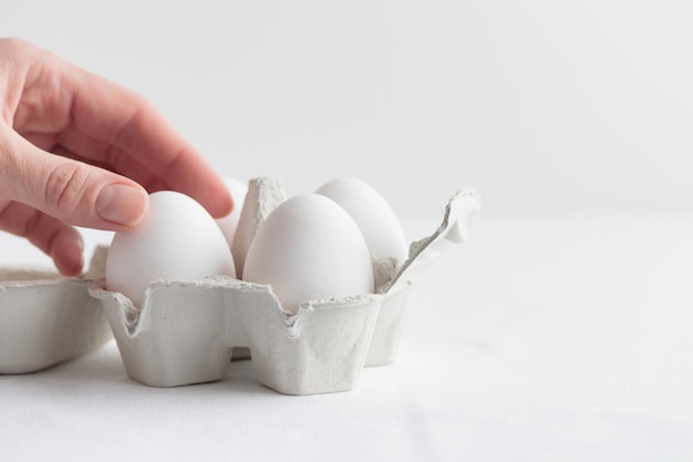 Witte eieren in een eierdoos met een hand op een witte tafel