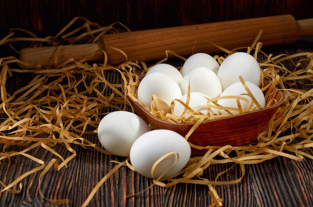 Witte eieren in een houten kom, op een papier rietje en een houten tafel. Op de achterkant van een deegroller. Low key.