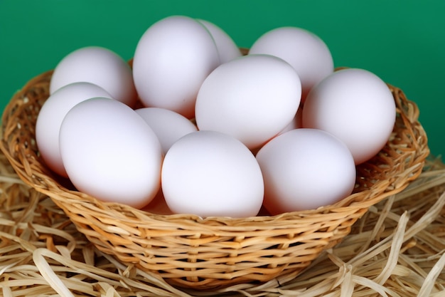 witte eieren in een rieten mand op stro op groene achtergrond close-up