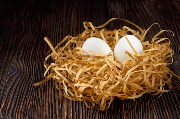 Witte eieren op papier stro in de vorm van een nest op een houten tafel. low key.