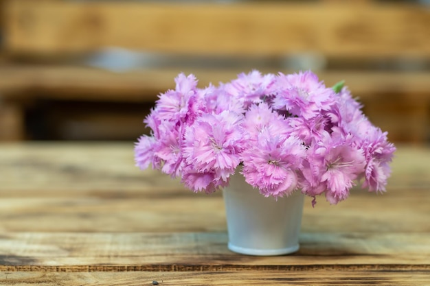 Witte emmer met pastelroze anjerbloemen op een houten tafel. Plaats voor een inscriptie.