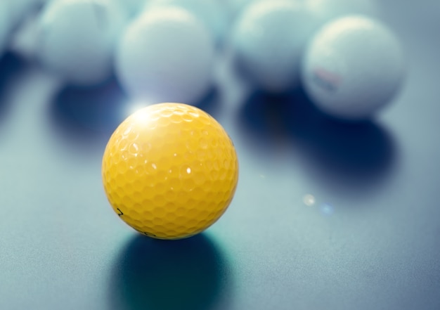 Witte en één gele golfballen op zwarte vloer. individualiteit en verschil concept.