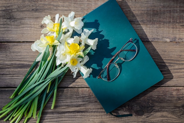 Witte en gele narcissen, boek en glazen op een houten tafel