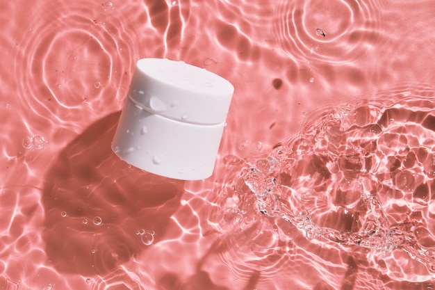 Witte en lege merkloze cosmetische zalfpot op het roze wateroppervlak Blanco label branding mockup Platliggend bovenaanzicht beauty spa medische huidverzorging en cosmetische lotion crème verpakkingsproduct