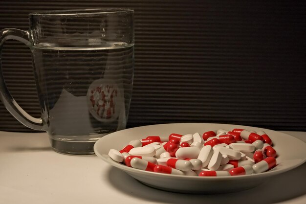 Witte en rode pillen in een bord een glas water close-up het concept van gezondheidsbehandeling