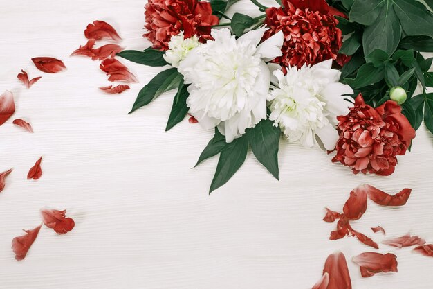 Witte en rode pioenrozen met gevallen bloemblaadjes op wit hout