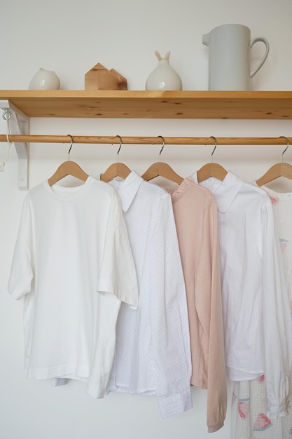 Witte en roze T-shirts hangen op houten hangers in de kamer.