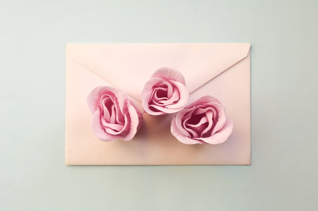 Witte envelop, drie roze roze bloemen op een blauwe achtergrond. Minimaal plat leggen