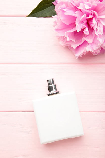 Witte fles parfum met roze bloem op roze achtergrond