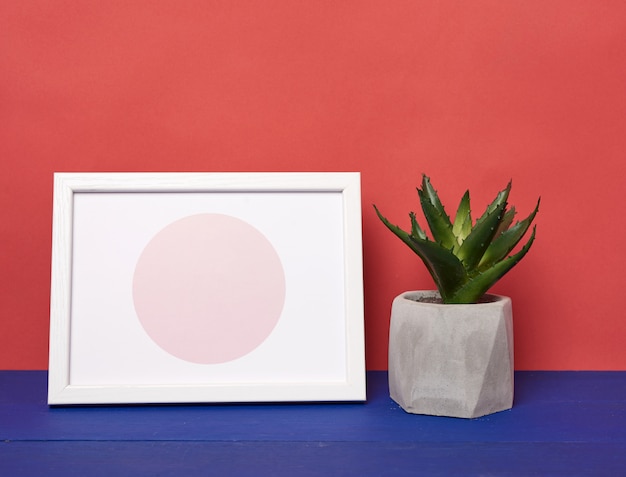 Witte fotolijst en keramische pot met een groeiende plant op een blauwe houten tafel