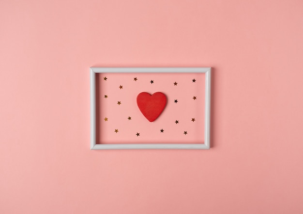Witte fotolijst met rood hart en gouden sterren binnen op de roze achtergrond. Valentijnsdag concept. Plat lag, bovenaanzicht.