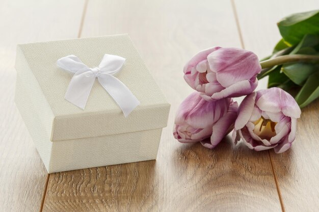 Witte geschenkdoos en lila tulpen op houten planken Wenskaartconcept