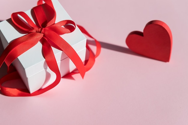 witte geschenkdoos met rode strik lint en rood hart op roze achtergrond voor Valentijnsdag