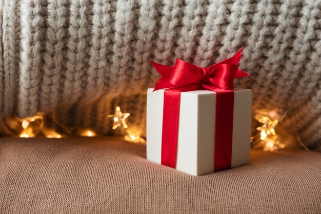 Foto witte geschenkdoos met rood lint strik op beige warme gebreide truien en kerstverlichting