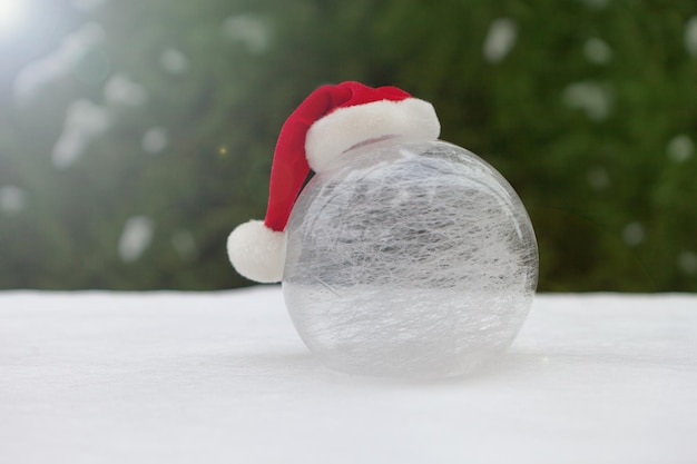 Witte glazen bal op sneeuw met kerstmuts winterwereld in de buurt van kerstboom besneeuwde achtergrond