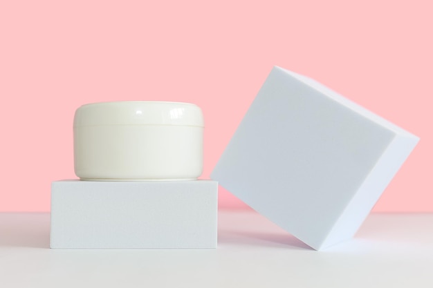 Witte glazen cosmetische pot met cosmetische crème voor lichaam en gezicht op een vierkant wit podium